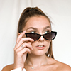 Person with long hair and sunglasses looking to the side against a white background.